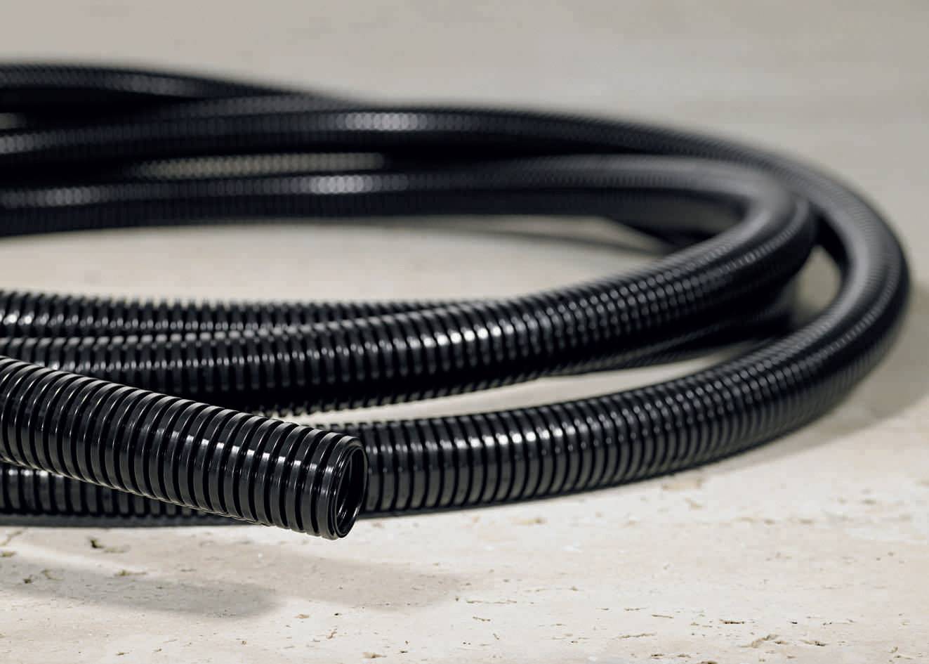 A black, flexible plastic hose lies on the ground. The hose is ribbed and appears robust, possibly for cable protection.