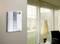 A modern intercom system mounted on the wall of a living room, with a window in the background illuminating the space.