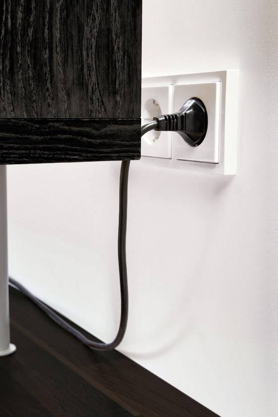 A black cable is plugged into a wall socket, running behind a dark wooden table.