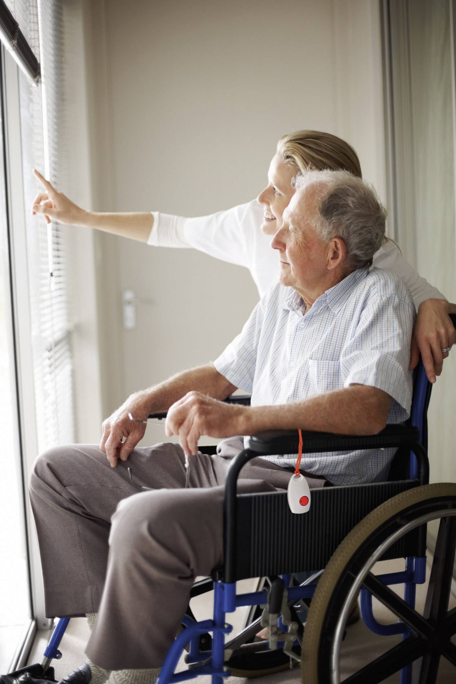 An older man in a wheelchair looks out of the window with a younger person. Both appear content and focused on something outside.