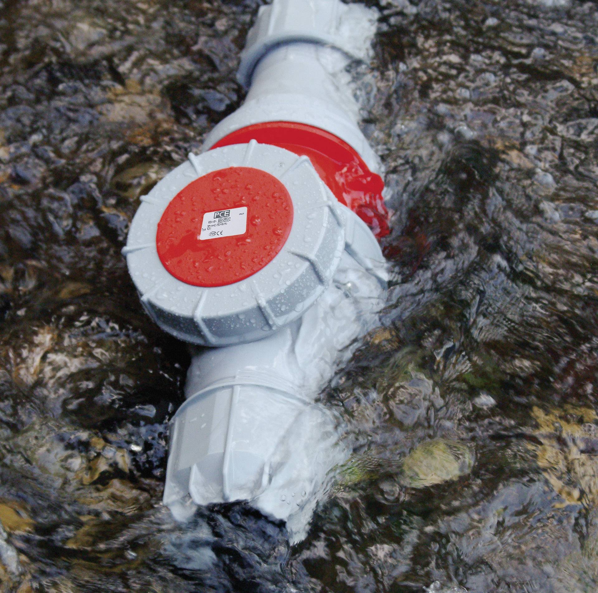 A grey pipe with a red valve floats in flowing water. It is half-submerged, with water currents visibly moving along its surface.