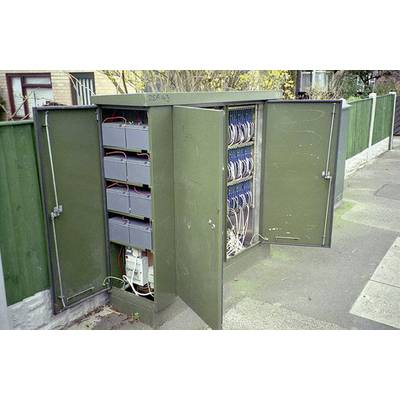 An open, green telecommunications distribution cabinet on a pavement reveals cables and various technical components within it.