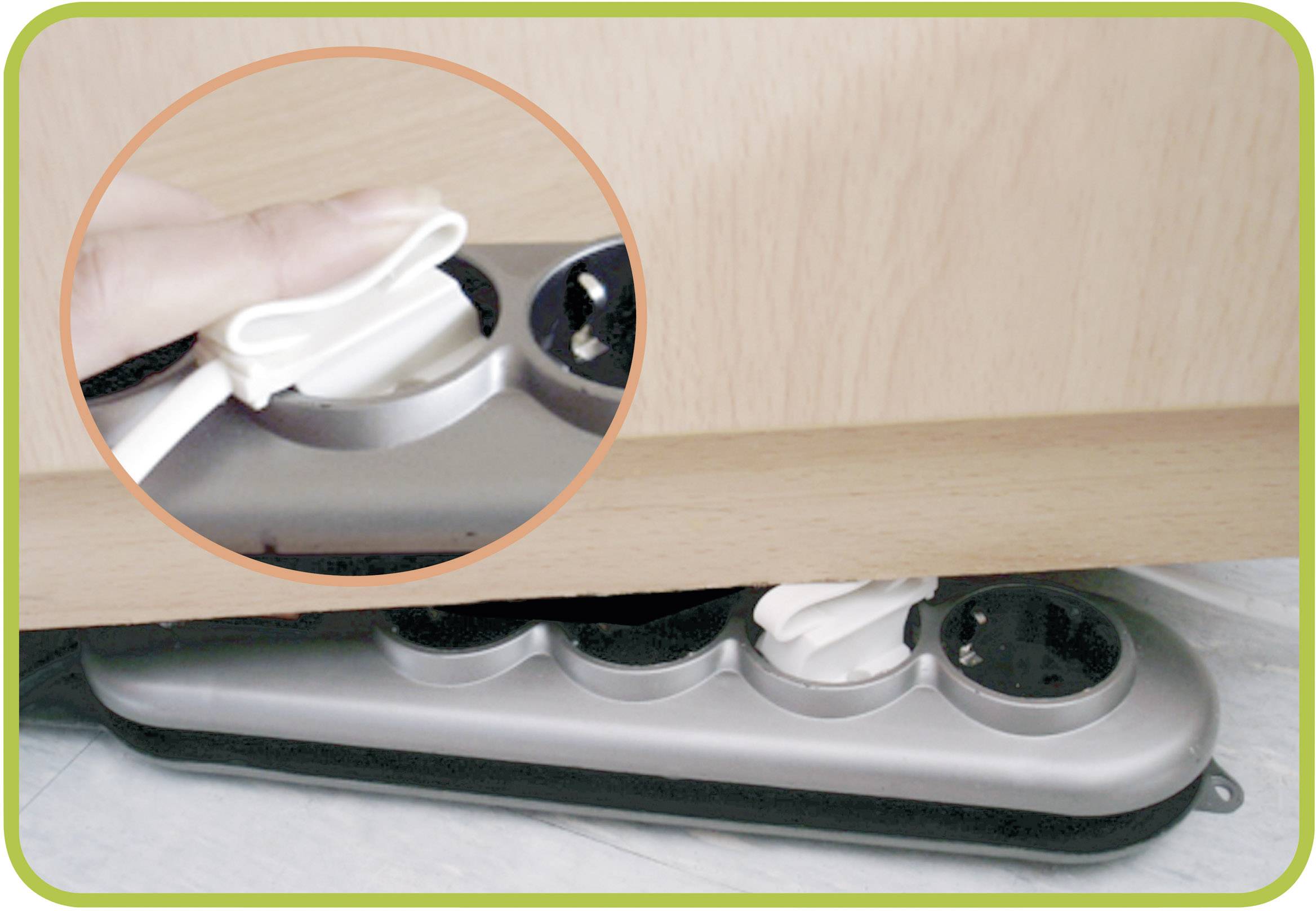 Close-up of a person positioning a plug adapter between a piece of furniture and a wall. In detail: Fingers pressing the adapter button.