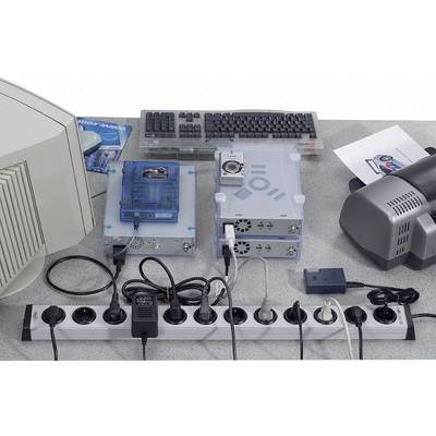 A desk with a monitor, keyboard, electronic devices and several cables plugged into a power strip.