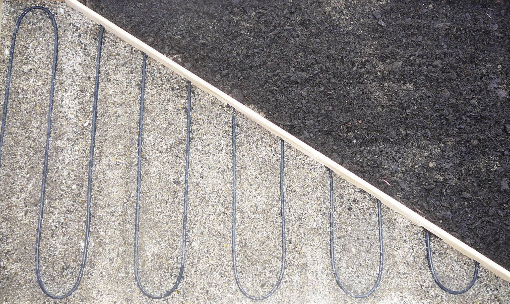 Heating mat under soil for gardening, visible on concrete on the left, covered with earth on the right.