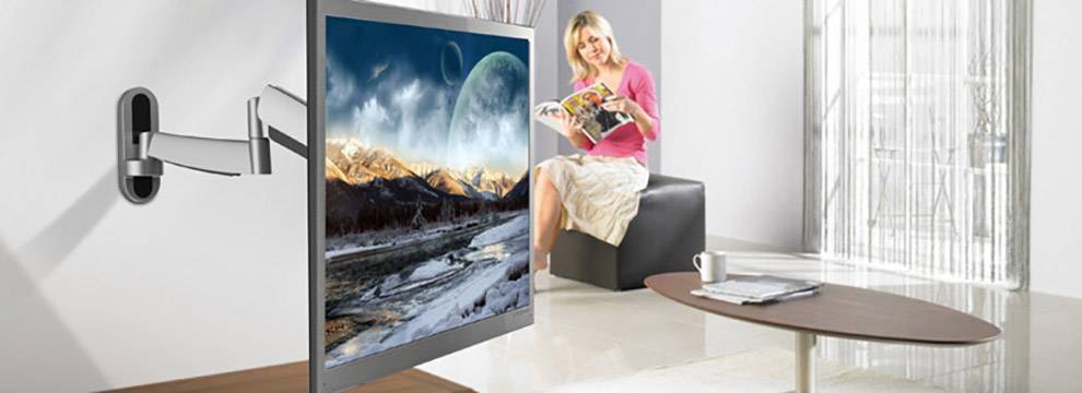 A person is sitting in an armchair in a modern living room, reading a magazine. A flat-screen television with a landscape scene is mounted on the wall.
