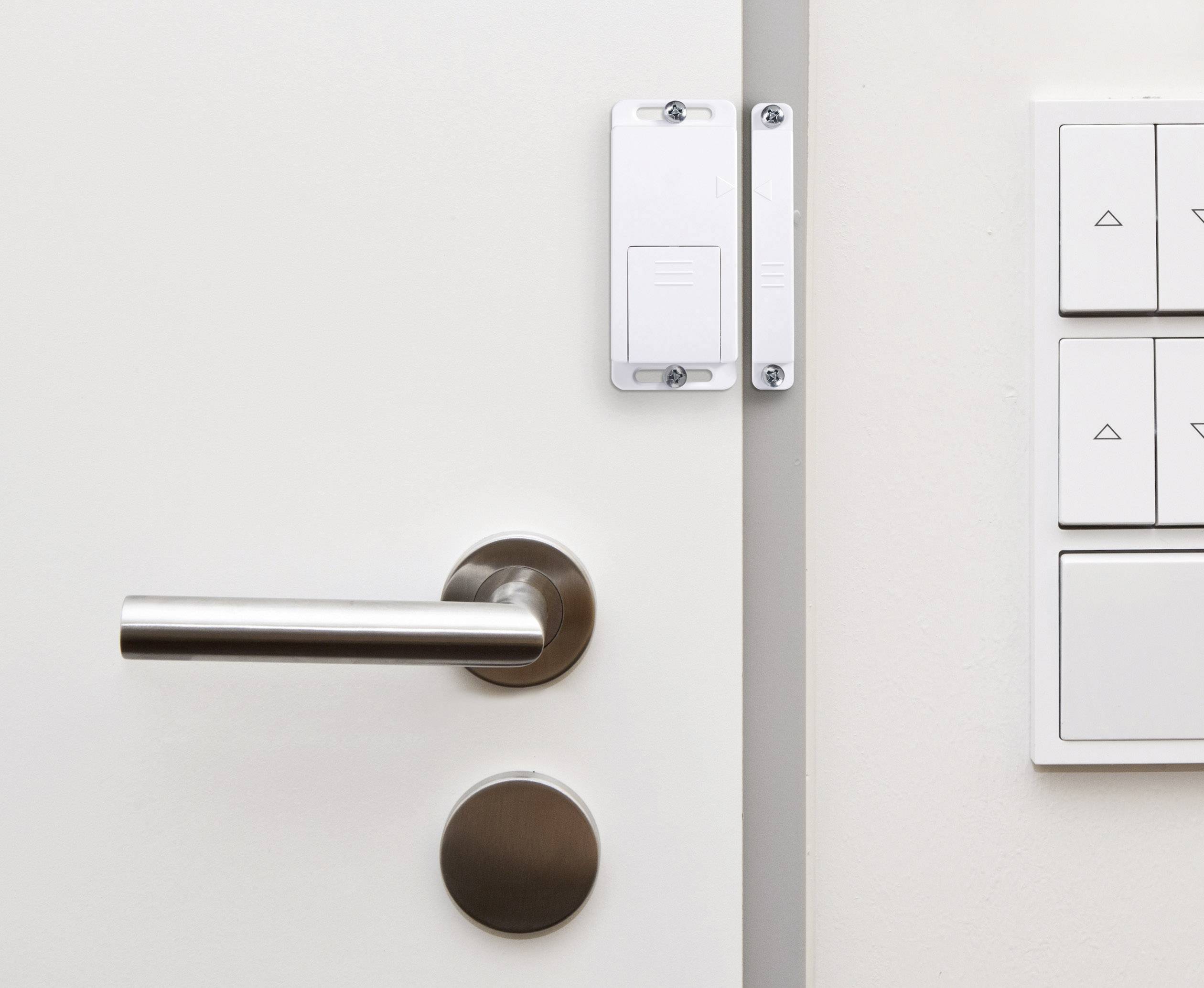 A white door with a stainless steel door handle on the left, with a light switch beside it on the wall.
