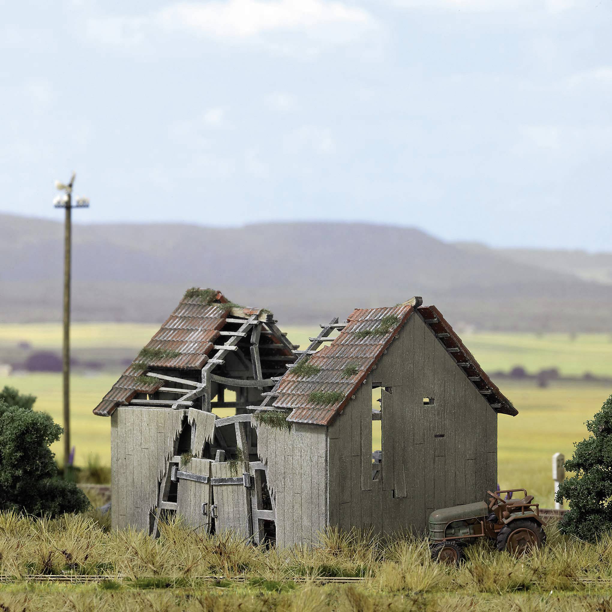 An old, dilapidated house on a field with a rusty tractor in the foreground, mountainous landscape in the background.