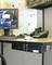 A desk with a computer, telephone and mouse. A world map hangs in the background. A headset lies beside the monitor.