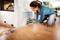 A woman is laying a laminate floor and cutting a piece to size with an electric jigsaw. Wooden strips and spacers are lying beside her.