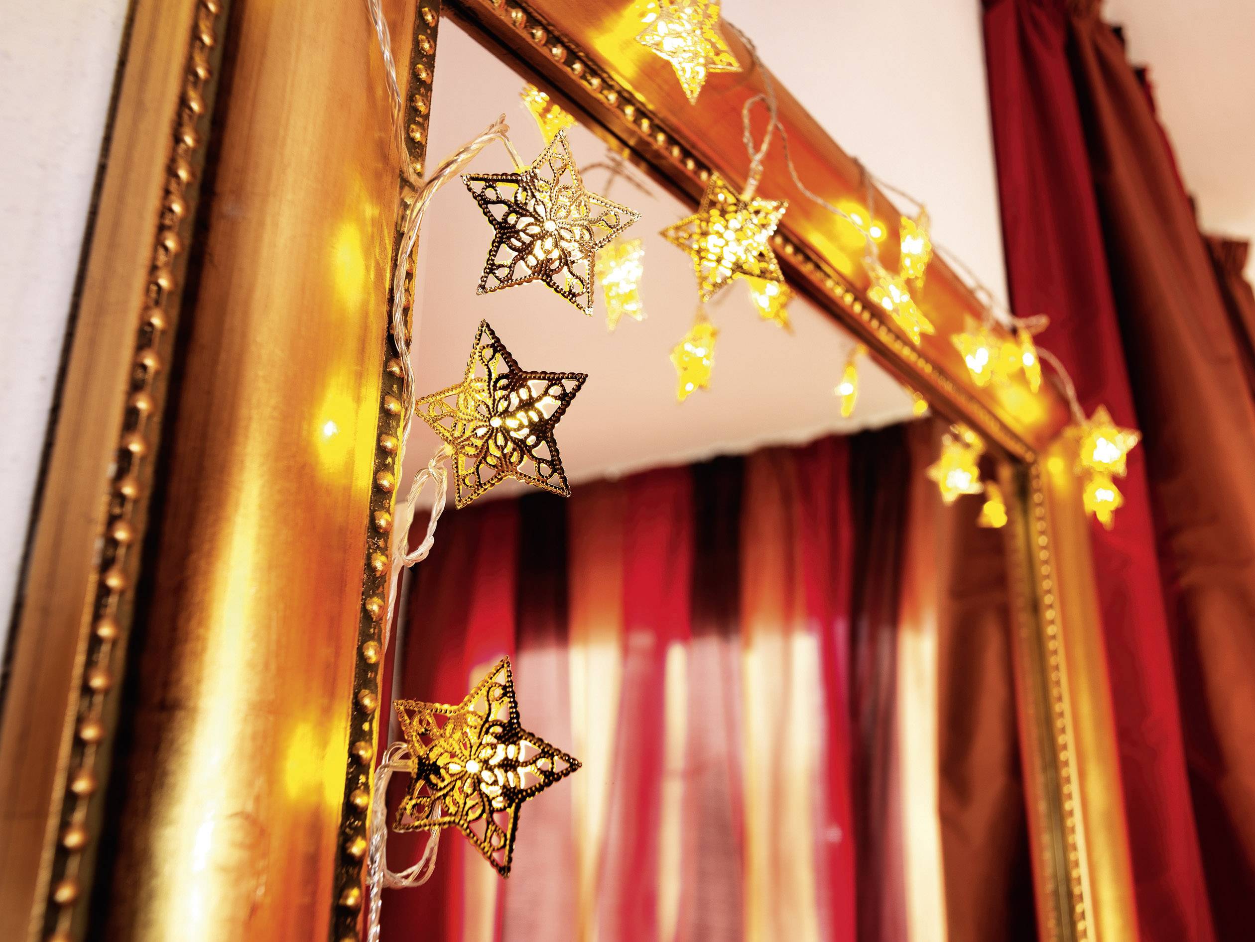 A mirror with a golden frame is adorned with glowing starry lights. Red curtains are visible in the background.