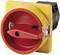 A red emergency stop button in a yellow housing. Used for safety shut-off of electrical equipment.