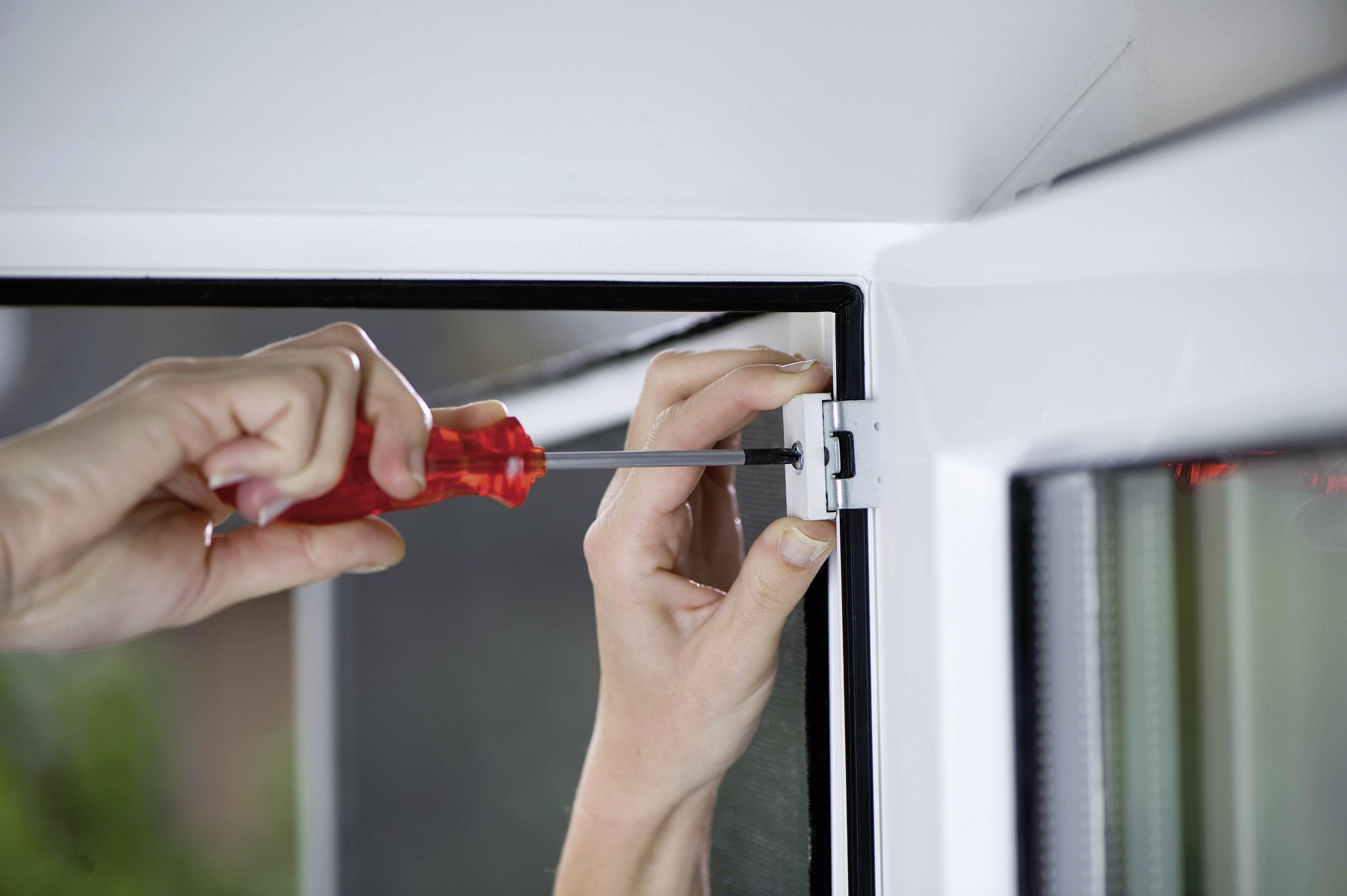 'Hands are repairing a window with a screwdriver, while a person tightens the hinge to ensure stability.'