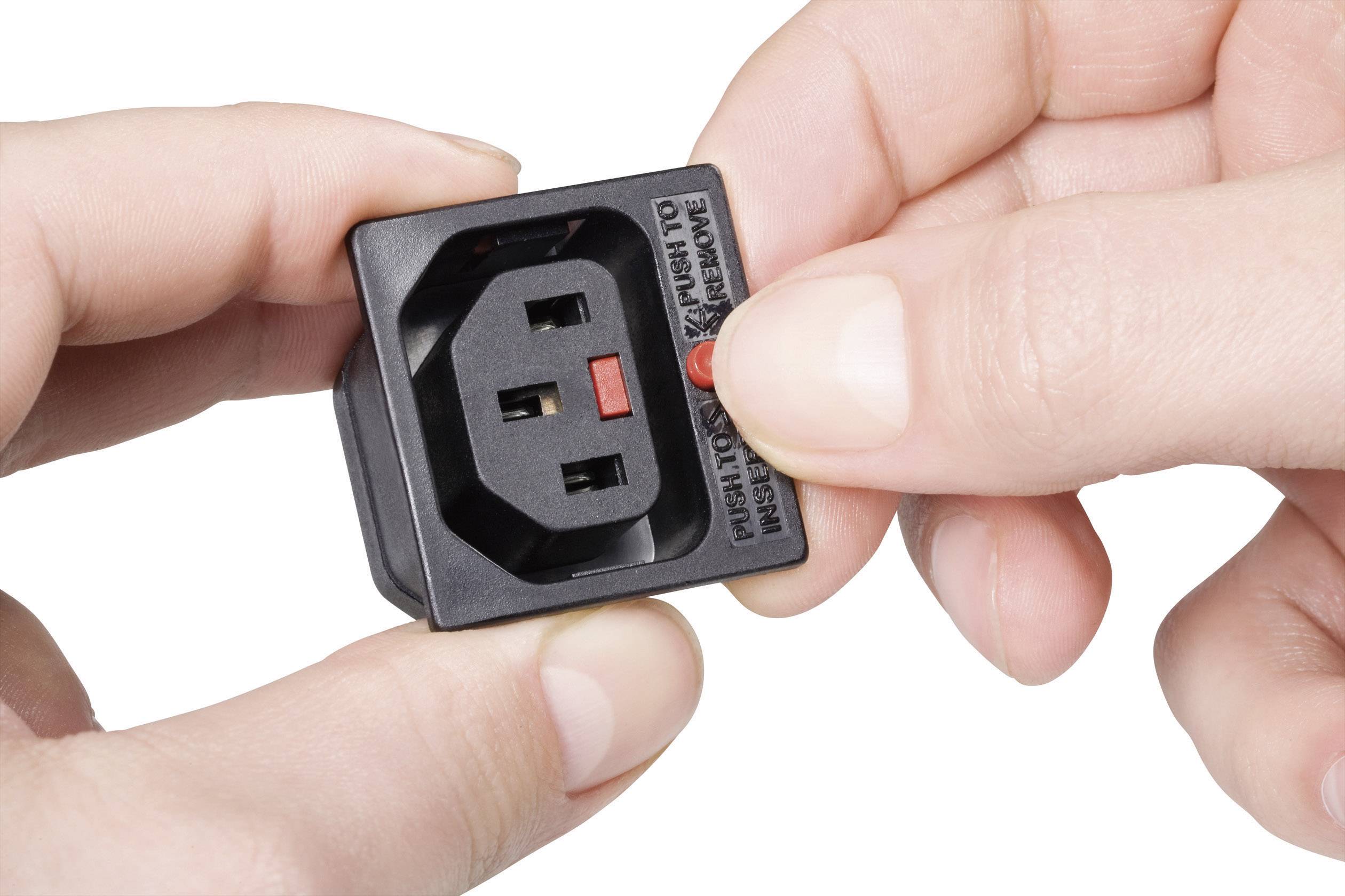 Two hands are holding a small black device with a socket. A fingertip is pointing to a red button or switch on the device.