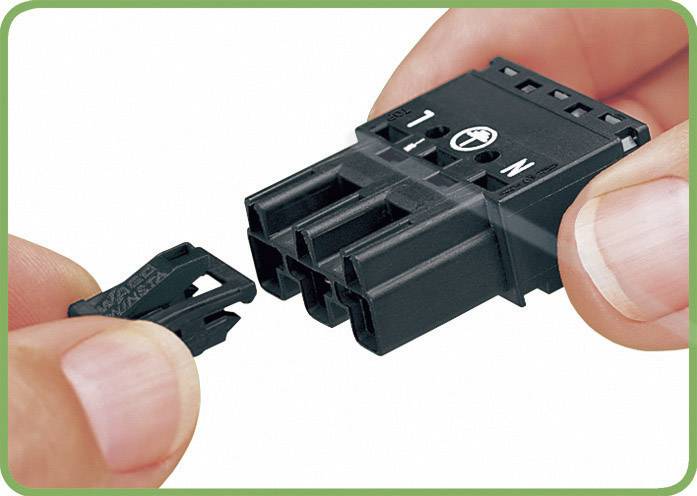 Two hands are connecting a black electrical connector. The left hand is holding a small clip, while the right hand holds the main plug.