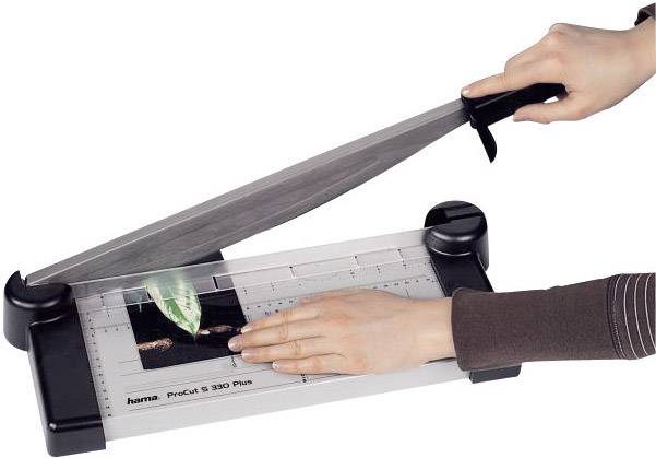 A person is cutting paper with a lever cutter. The paper shows an image of a green leaf.