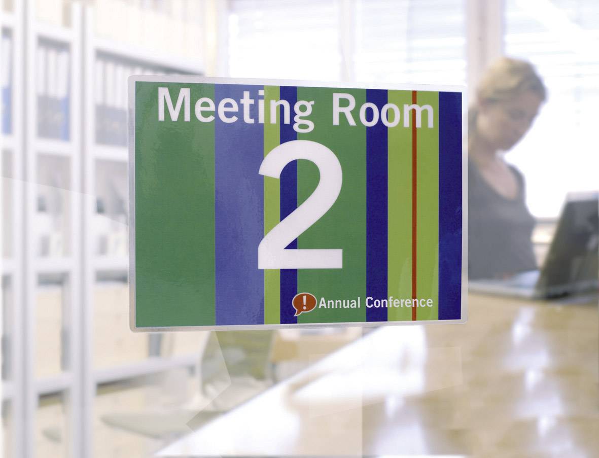 A sign reading 'Meeting Room 2' and 'Annual Conference' on a striped background. A blurred person is visible in the background.