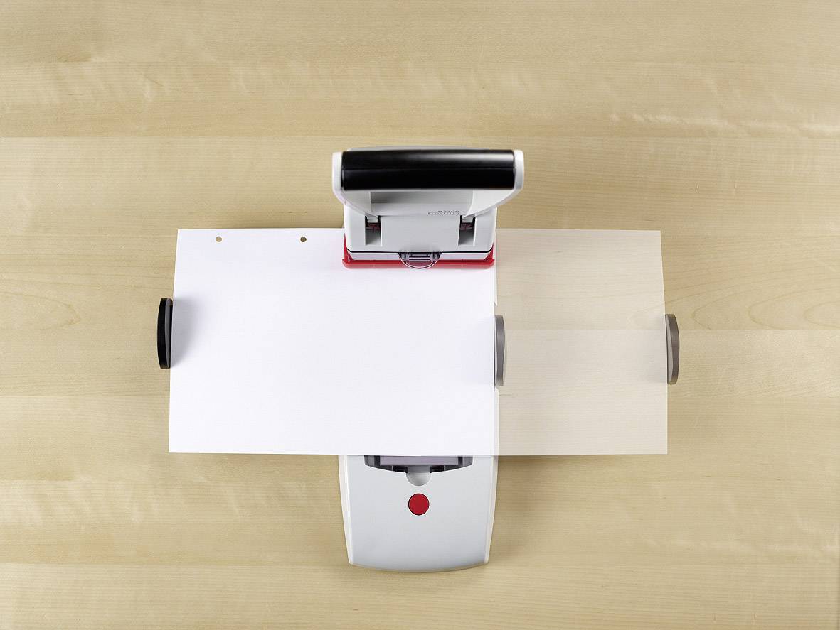 A document is being punched by a hole punch. The hole punch is placed on a wooden table.