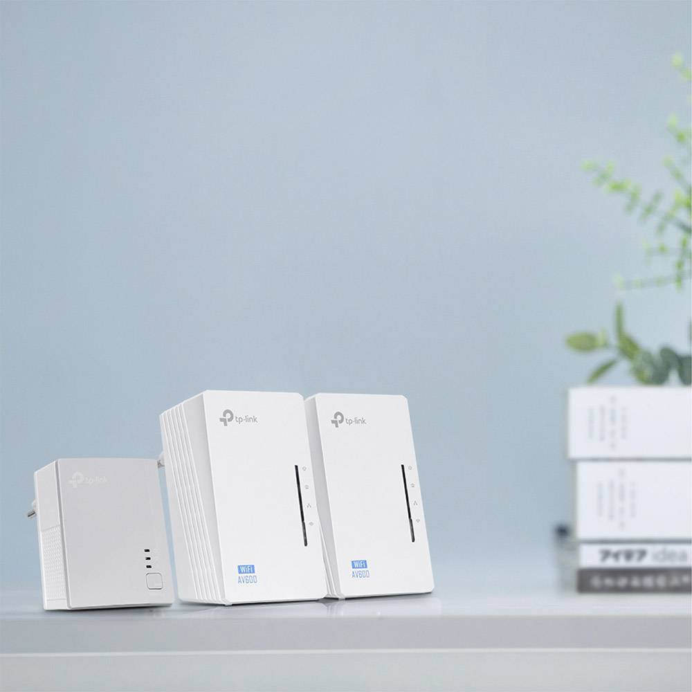Three white Wi-Fi adapters on a table in front of a blue wall. Books and a plant are visible in the background.