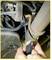 A person is using a tool to work on a component beneath a vehicle. The focus is on the hand holding a spanner.
