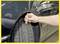 A hand measures the tread depth of a car tyre with a tread depth gauge. The car is navy blue.