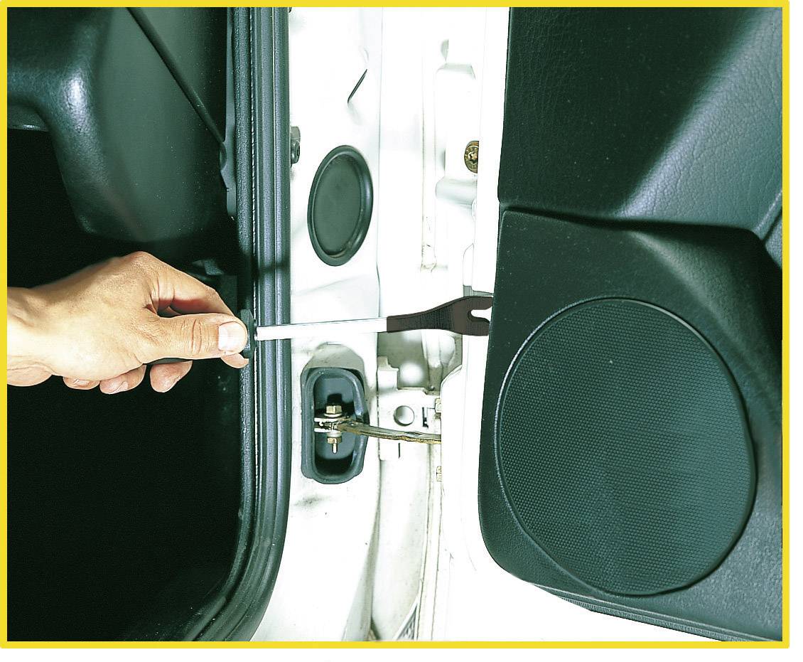 A hand is holding a screwdriver and is unscrewing a car door panel. The door is partially open, with the speaker visible.