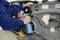 A person is repairing a car part in a workshop. Their hands are holding tools and are focused on an interior door panel.