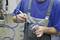 A worker wearing blue dungarees is cleaning a metal component with compressed air in a workshop environment.
