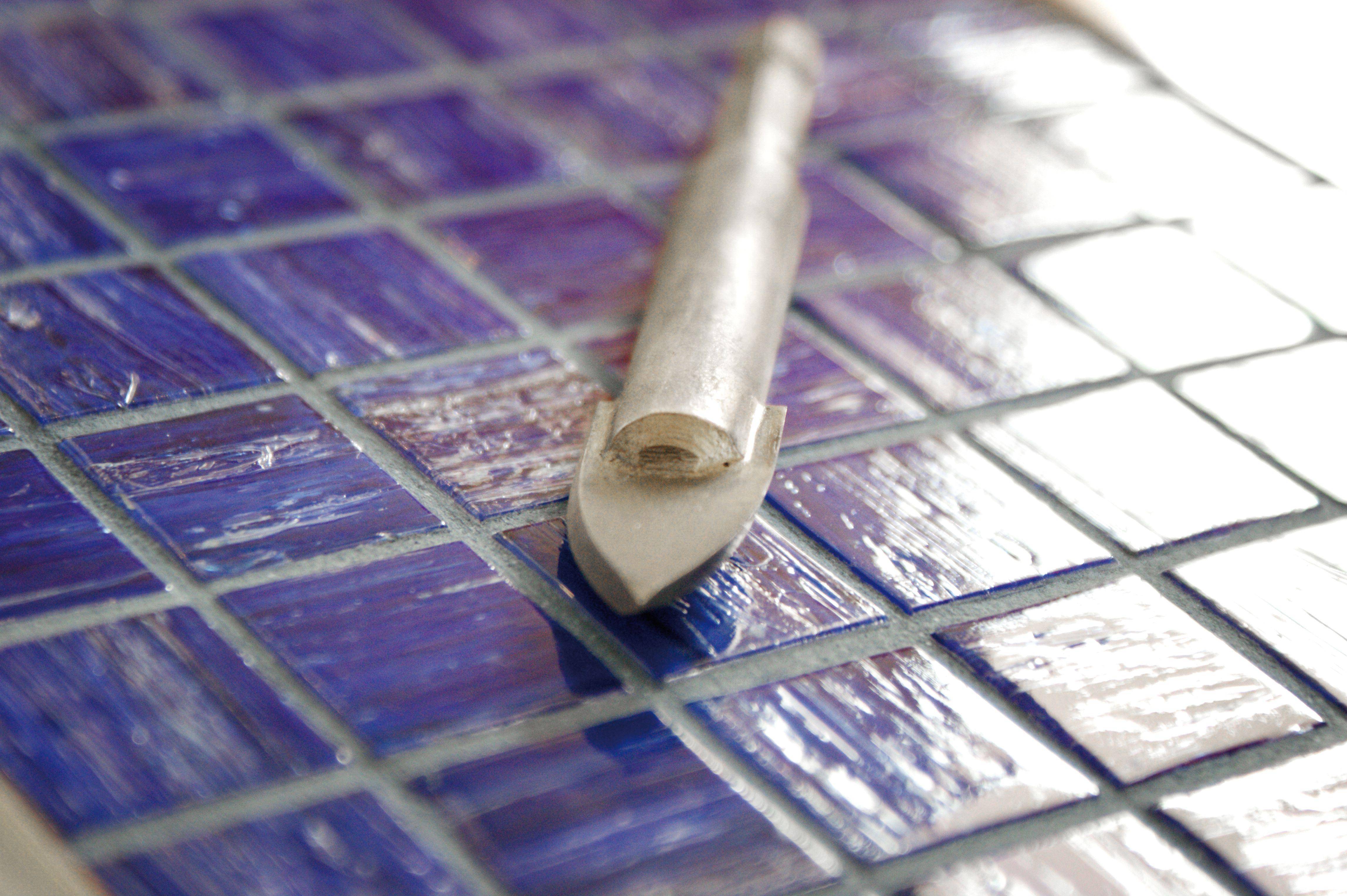 Tile cutter positioned on a blue mosaic tile, ready to cut. Building materials often used for creative or practical projects.