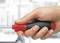 A hand is holding a screwdriver with a red handle. The background is out of focus.