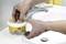A person is dispensing hand wash paste from a white container next to a sink. The paste is used for cleaning hands.
