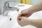 A person is washing their hands under running water at a sink.