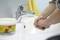 A person is washing their hands under a tap. Next to them is a tin of hand cleansing paste.