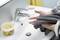 A person is wiping their hands with a grey towel beside a sink with a tap and a container of cleaning solution.