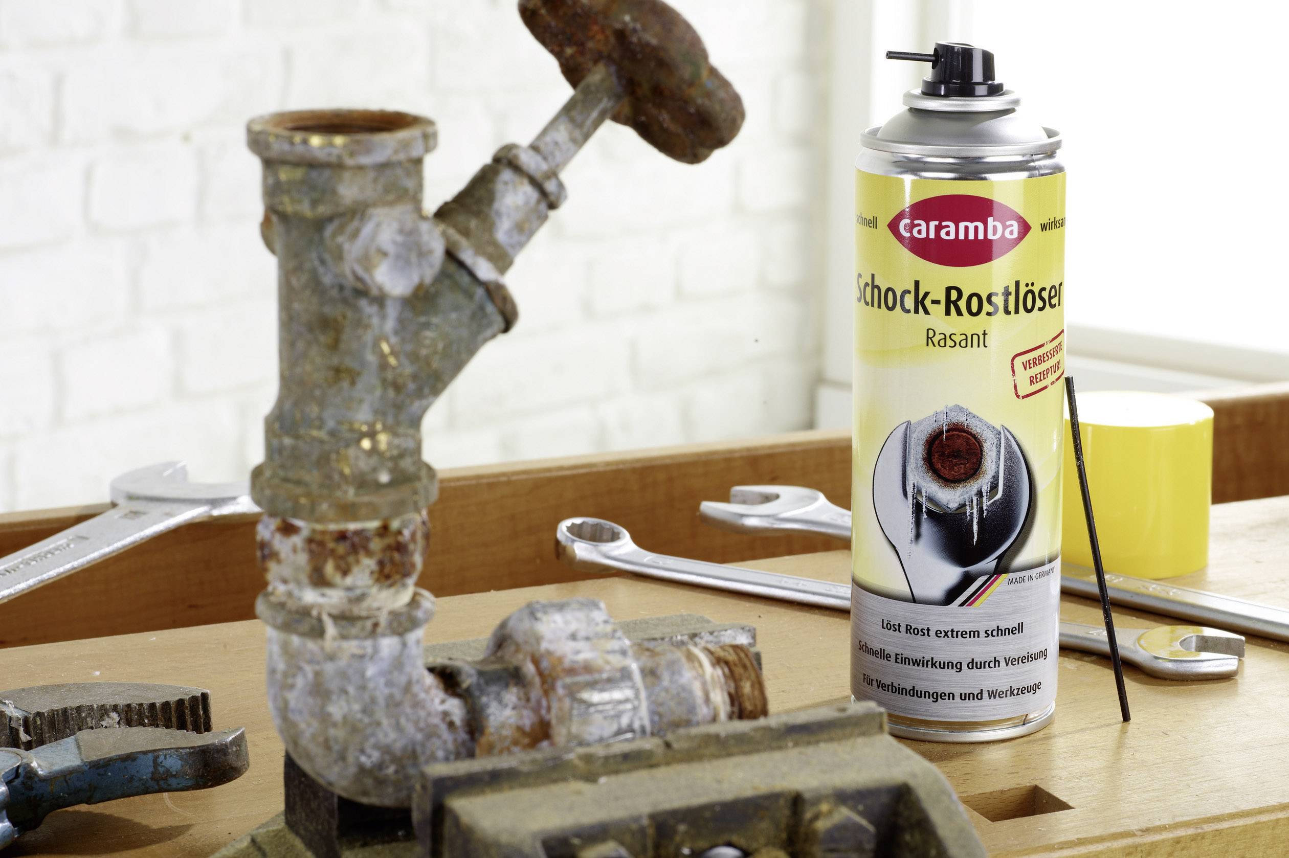 Old, rusted pipe in front of a can of rust remover by the brand 'Caramba'; surroundings show tools on a workbench.