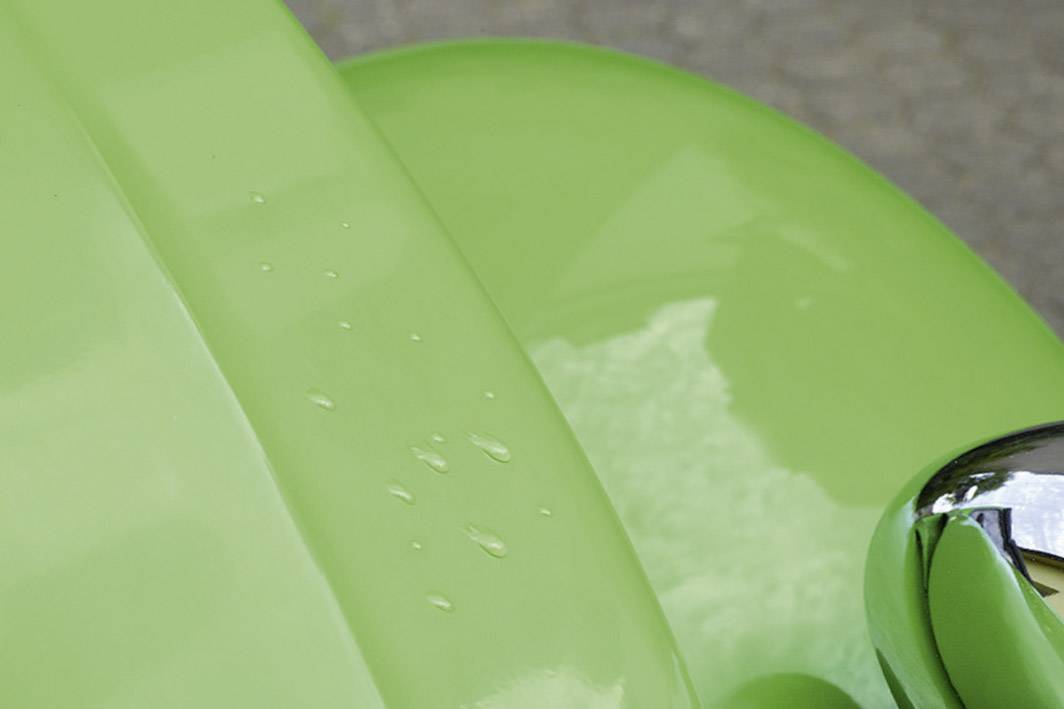 A close-up of a gleaming, light green car part with water droplets visible on its surface.