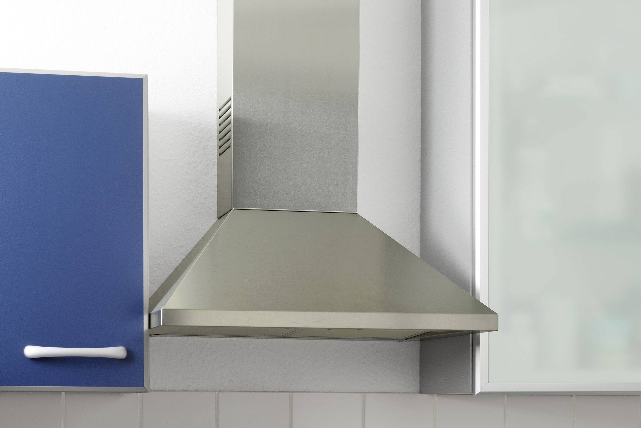 A stainless steel cooker hood mounted between a blue cabinet and a glazed surface in a modern kitchen.
