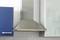 A stainless steel cooker hood mounted between a blue cabinet and a glazed surface in a modern kitchen.