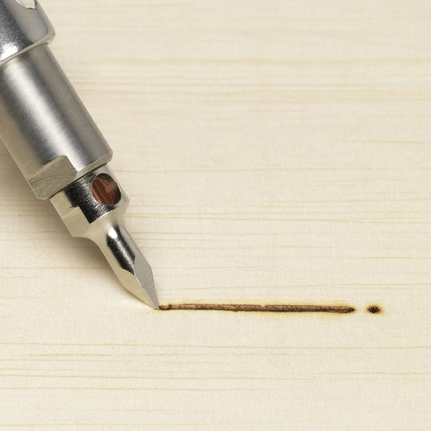 Close-up of a writing quill drawing a fine line of ink on a light wooden board.
