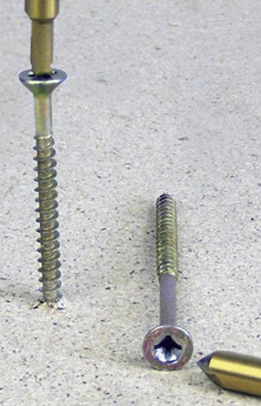 Two metal screws on a surface in different orientations. One screw is pointing upwards, the other lying flat.