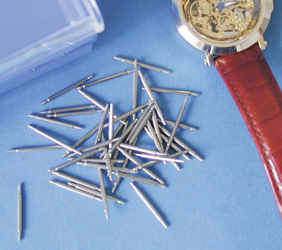 A wristwatch without a strap placed on a table next to a group of metal pins, possibly spare parts for watch straps.