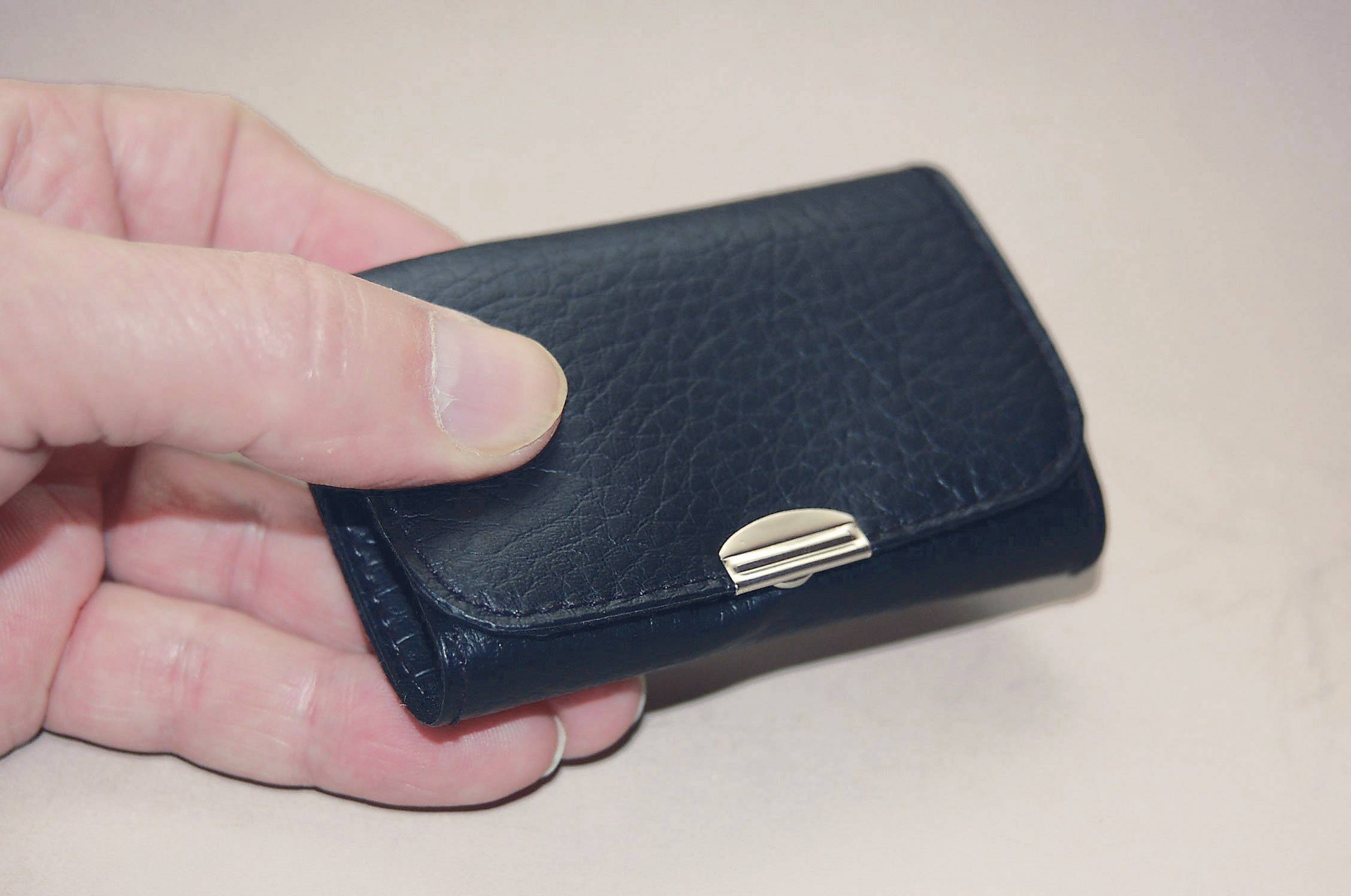 A hand is holding a black, structured leather case with a metal clasp.
