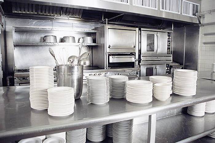 Clean, stacked plates on a stainless steel counter in an industrial kitchen demonstrate an organised and prepared working environment.