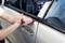 A person opens a car window with a red tool. The car is silver, and the interior is visible.