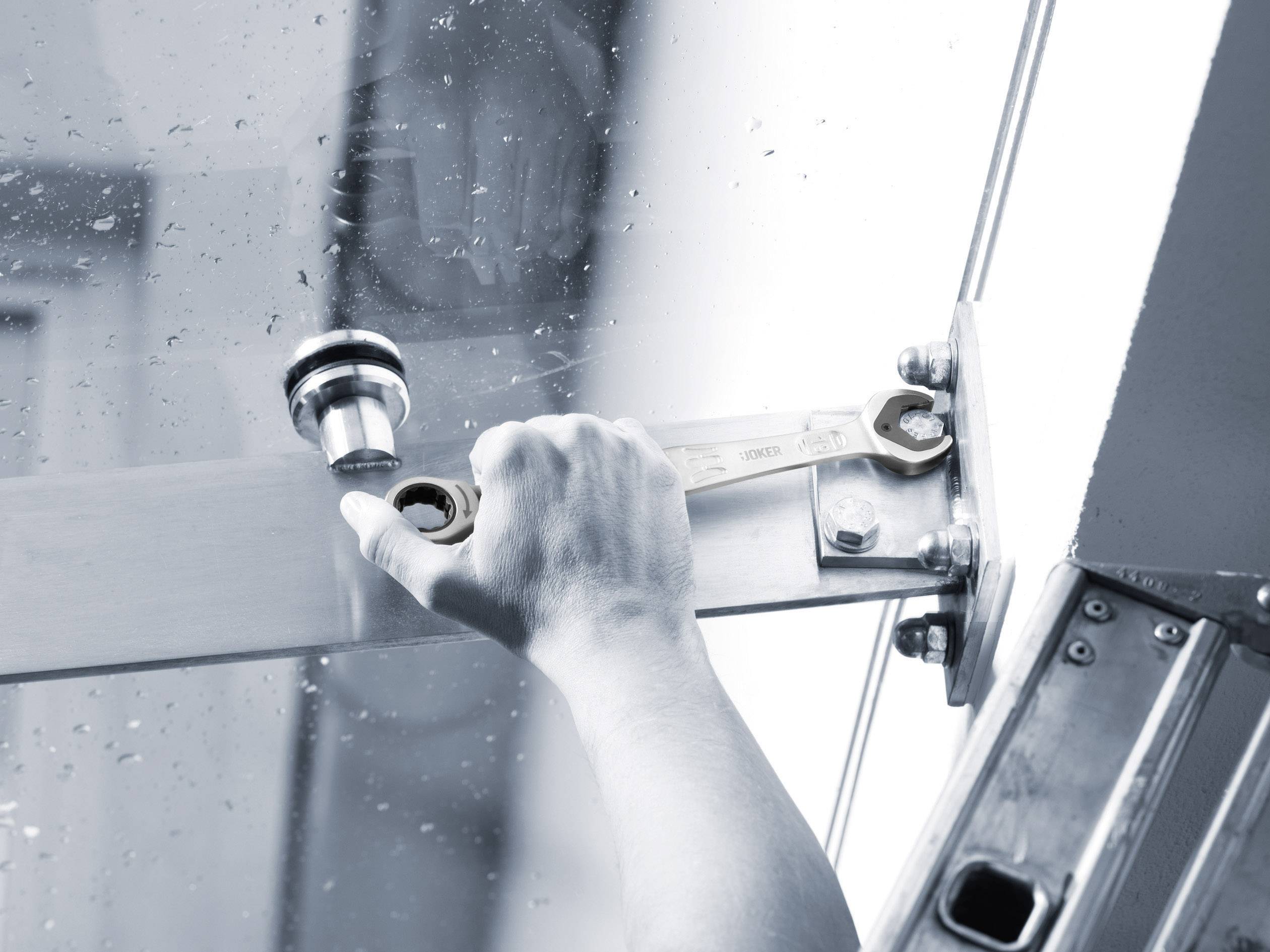 A hand using a spanner to adjust a glass door, possibly during installation or repair.