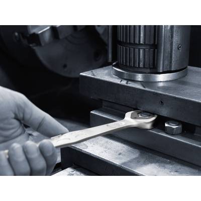 A hand holds a spanner on a machine. The focus is on precise adjustment and maintenance of machine components.