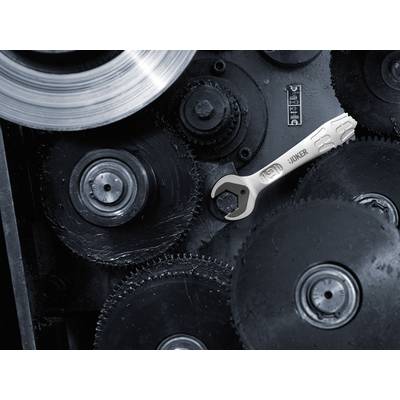A silver spanner lies on a large cogwheel in a mechanism comprising several interlocking gears.
