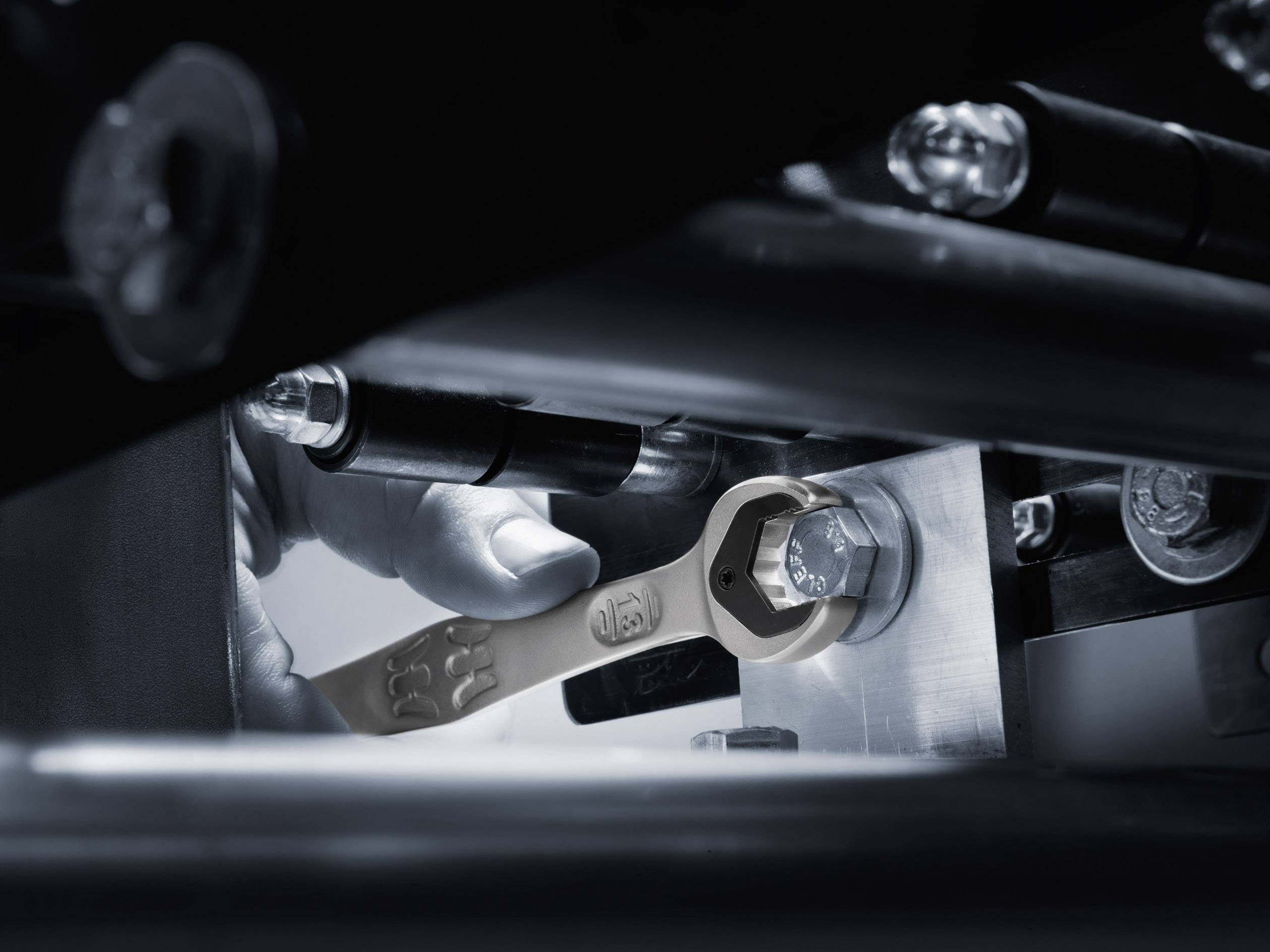 Close-up of a spanner tightening a screw in a machine. A hand is holding the spanner in a workshop environment.