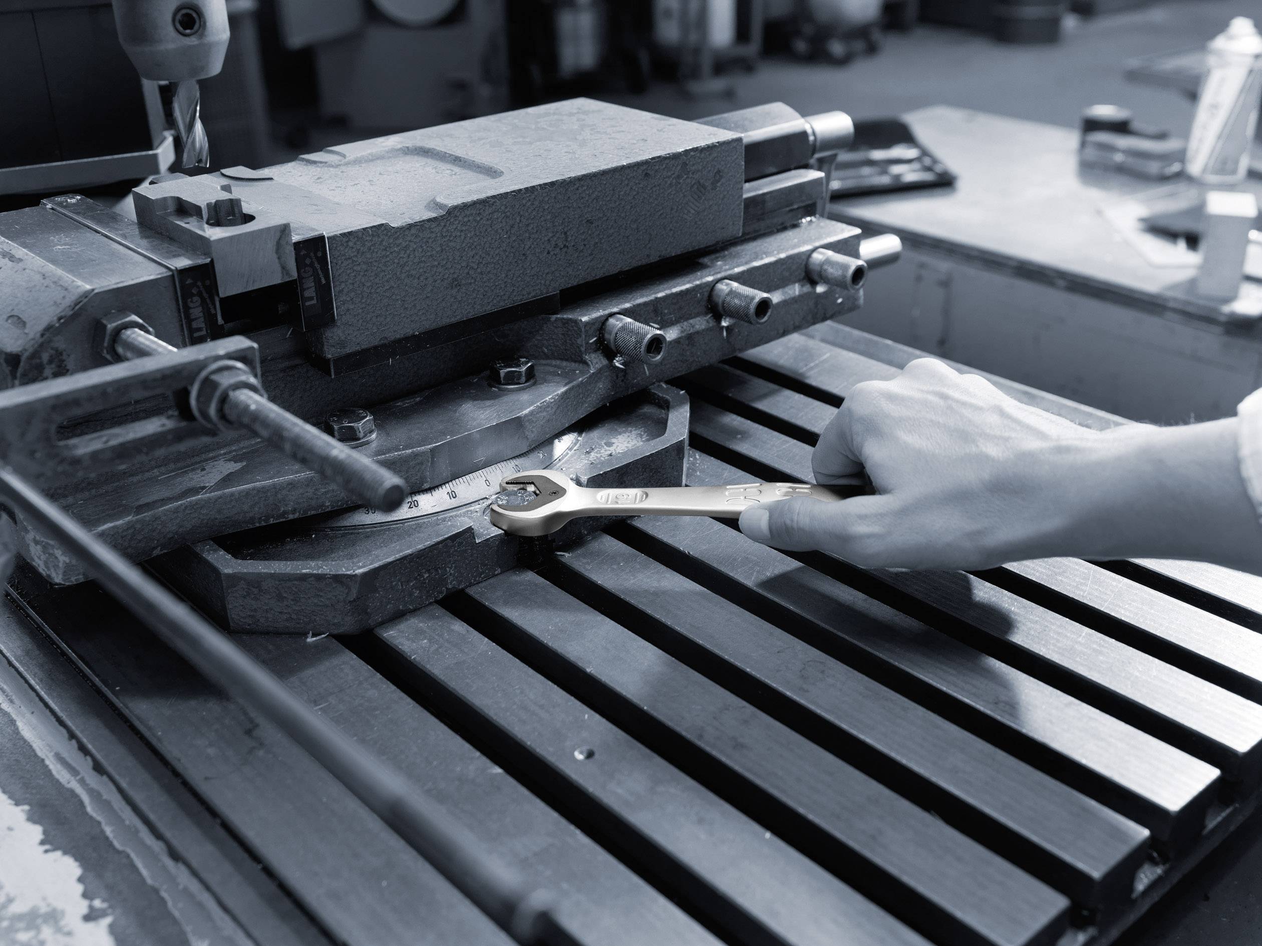 A person is working with a spanner on a metal machine. The workplace has an industrial ambience.