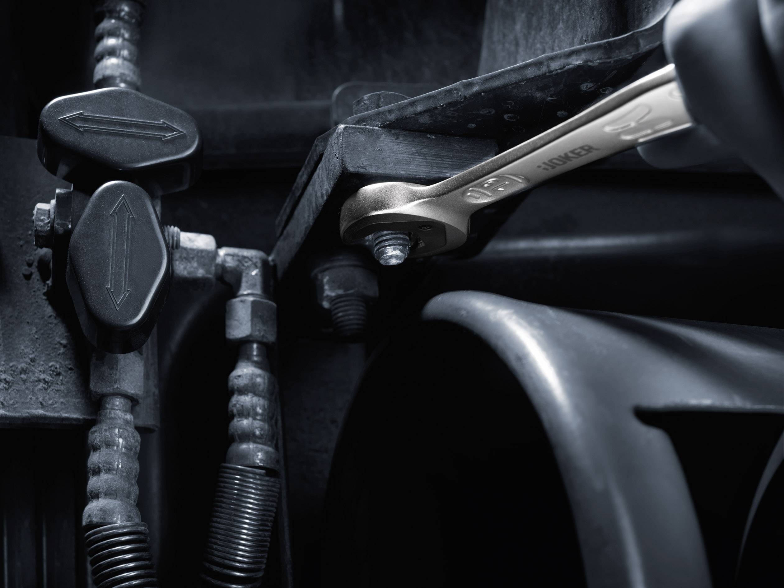 A spanner tightens a nut on a machine. Pipes and arrows on valve switches are visible.